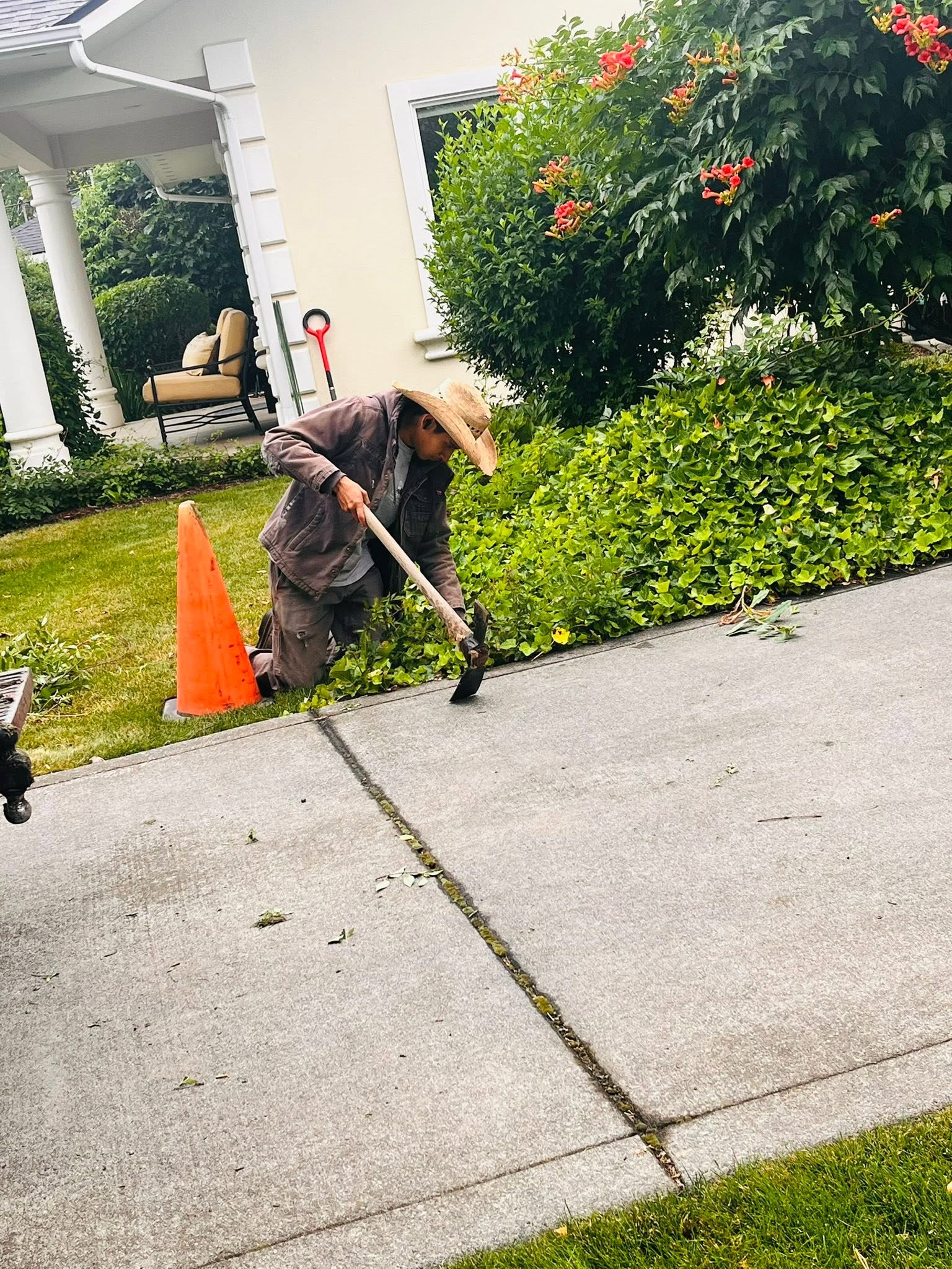 A Diaz Yard Care crew member edging a hedge line along a driveway